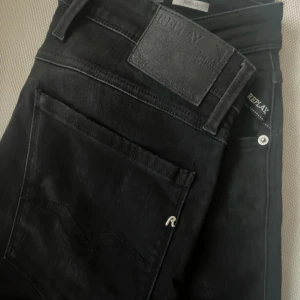  Replay Anbass jeans svarta - Säljer ett par svarta Replay Anbass jeans med      W32 L34 som knappt andvända och köptes för 1700. Men klassisk femficksdesign och snygga detaljer som logotyp på bakfickan och läderpatch i midjan. Jeansen har en slim passform och är tillverkade i mjukt stretchigt bomullsmaterial för extra komfort. 