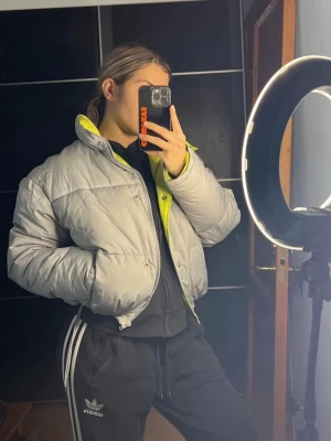 Grå pufferjacka med neongrön insida - Säljer en riktigt snygg pufferjacka i ljusgrått med en cool neongul insida. Jackan har hög krage, dragkedja och en oversized passform som ger en chill vibe. Perfekt för kalla dagar när du vill sticka ut lite extra. Använd 1 gång. 