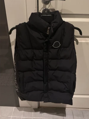 Svart dunväst från Moncler S - Säljer en svart dunväst från Moncler i storlek S. dragkedja framtill och två fickor. Moncler-logga på bröstet och tryckt text på sidan. Perfekt för lager-på-lager och riktigt snygg till höst och vinter.