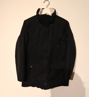 McKinley vinterjacka - Svart parkajacka från McKinley med mjukt, ljust teddyfoder och snygg fuskpäls runt huvan. Jackan har praktiska fickor med knappar och lång ärm. Perfekt för kalla dagar med sin varma och sköna insida. Exodus Active Elements-detalj på ärmen.