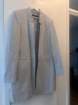 Ljusgrå kavaj från Vero Moda - Säljer en stilren ljusgrå kavaj från Vero Moda i storlek 40. Kavajen har en rak passform, diskreta fickor framtill och stängs med en knapp. Materialet är mjukt och känns bekvämt, perfekt för dig som gillar en clean och enkel look.