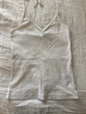 Vit halterneck topp från Gina Tricot - Säljer en enkel och stilren vit topp från Gina Tricot. Toppen har smala axelband som knyts i nacken