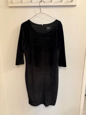 Svart sammetsklänning från Amazing - Supersnygg svart sammetsklänning med trekvartsärm och rund halsringning. Klänningen har en figurnära passform och dragkedja bak. Perfekt för dig som vill ha en stilren look med lite lyxig känsla.