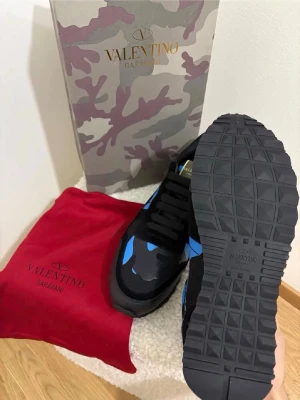 Valentino Rockrunner  - Säljer ett par Valentino Rockrunner sneakers i svart med blå och grå camouflagemönster. Skorna har snörning, robust sula och detaljer i skinn och textil. Kommer med originalkartong och röd dustbag. Perfekta för dig som vill sticka ut med exklusiva sneakers.