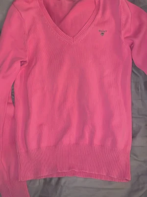 Rosa v-ringad tröja från Gant - Säljer en rosa v-ringad tröja från Gant med diskret logga på bröstet. Tröjan har långa ärmar och ribbade muddar vid ärmslut och nederkant. Perfekt för dig som vill ha en färgglad och stilren look. Pris kan diskuteras 