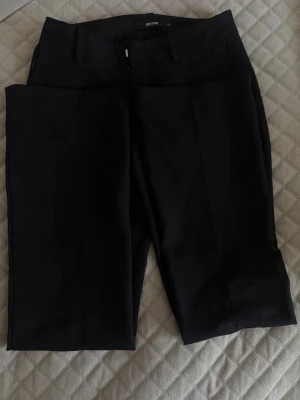 Svarta kostymbyxor från Bik Bok - Säljer de virala vera low waist svarta kostymbyxor från Bik Bok med klassisk rak passform och pressveck. Byxorna har hällor för bälte och är tillverkade i ett mjukt, vävt material som ger en clean och stilren look. Perfekta till en snygg topp eller skjorta.