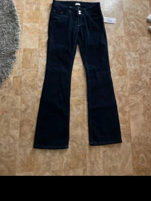 Mörkblå manchesterbyxor från Nelly - Snygga mörkblå manchesterbyxor från Nelly med låg midja och bootcut-snitt. Byxorna har dubbla knappar framtill, kontrastsömmar och coola detaljer på bakfickorna. Perfekta för dig som vill ha en retrovibe och skön passform.