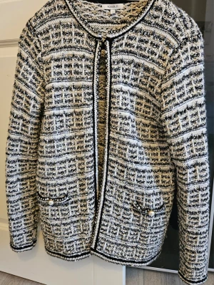 Rutig cardigan jacka från Rosebud - Säljer en snygg rutig cardigan jacka från Rosebud i svart, vit och beige. Jackan är stickad med dekorativa pärlknappar på fickorna och har en klassisk, lite boxig passform. Perfekt för dig som vill ha en chic och trendig look.
