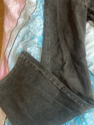 Svarta Perfect Jeans med fickdetaljer - Säljer ett par svarta jeans från Gina Tricot  i storlek 34. De har raka/utsvängda  ben, coola fickor med lock och knapp bak samt klassisk femficksdesign fram. Jeansen är i ett mjukt denimtyg och har en snygg tvättad look.