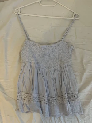 Ljusblå smockad linnetopp 157 XS - Supersöt ljusblå linnetopp från 157 i storlek XS. Toppen har smock upptill, tunna justerbara axelband och fina virkade spetsdetaljer nertill. Perfekt till sommaren och ger en luftig och chill vibe.