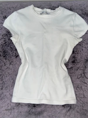 Vit basic t-shirt från Bershka - Enkel och stilren vit t-shirt från Bershka. Modellen är kortärmad med rund hals och har en klassisk passform som funkar till allt. Perfekt att matcha med jeans eller kjol för en clean look.