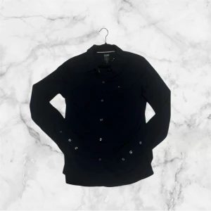 Svart skjorta från Hilfiger Denim - Klassisk svart skjorta från Hilfiger Denim med lång ärm och knappar framtill. Skjortan har en diskret logga på bröstet och är tillverkad i mjuk bomull. Perfekt till jeans eller chinos för en clean look.