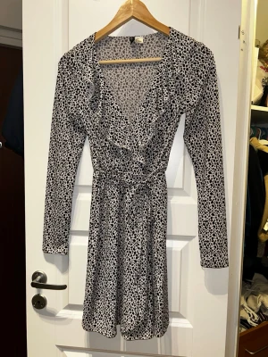 Leopardmönstrad omlottklänning H&M - Snygg kort leopardmönstrad omlottklänning från H&M med volangdetaljer och knyt i midjan. Klänningen har lång ärm och v-ringning, perfekt för dig som gillar att sticka ut. Materialet är mjukt och lätt, vilket gör den superbekväm.