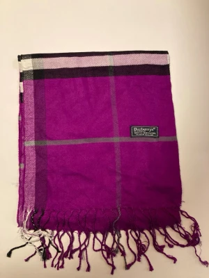 Lila rutig halsduk från Burberrys - Vi säljer denna otroligt snygga burberry halsduk utan defekter med färgerna lila, vit, svart och lite grön