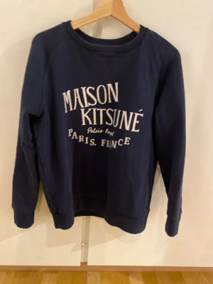 Mörkblå Maison Kitsuné sweatshirt M - Snygg mörkblå sweatshirt från Maison Kitsuné med vit text på bröstet. Klassisk rund halsringning och långa ärmar. Tillverkad i mjuk bomull, perfekt för en chill och stilren look.