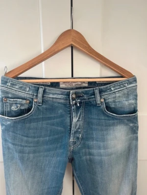 Jacob Cohen jeans  - Säljer ett par Jacob Cohen jeans i ljusblå tvätt med snygga slitningar och klassiska fem fickor. Jeansen har tapered passform, normal midja och är gjorda i mjukt stretchigt denim. Bakfickorna har Replay-logga och coola detaljer. Perfekta för en chill och stilren look.  Strl 36 men sitter som 32 i midja i modellen 688