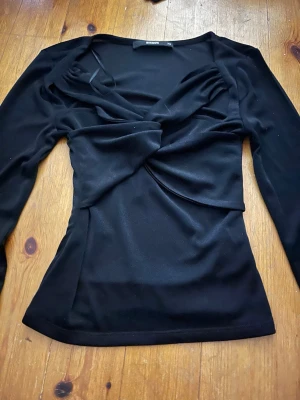 Svart topp från BikBok - Säljer en svart omlottopp från BikBok i storlek XS. Toppen har långa ärmar och en snygg twistad omlottdetalj frampå. perfekt till många olika outfits. Köpt på vinted men har själv aldrig använt då den var förliten. Hör gärna av dig vid fler frågor ❤️ (kan ej visa hur den sitter på, då den som sagt är för liten.)