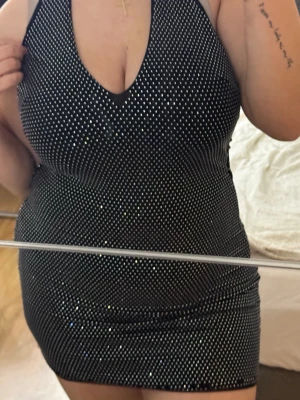 Glittrig svart kortklänning Amisu - Supersnygg svart kortklänning från Amisu med glittriga stenar över hela tyget. Djup v-ringning och ärmlös design som ger en riktigt partyvibe. Klänningen har figurnära passform och dragkedja i ryggen. Perfekt för dig som vill sticka ut!