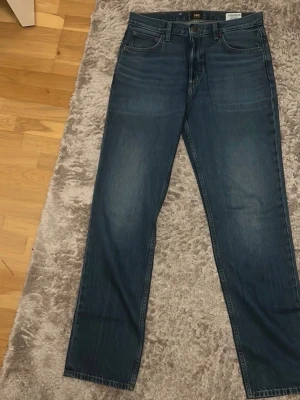 Mörkblå Lee jeans straight fit - Säljer ett par mörkblå jeans från Lee med klassisk femficksdesign och raka ben. Jeansen har en snygg tvätt och tydliga Lee-detaljer på bakfickan och linningen. Tillverkade i slitstarkt denimtyg som ger en tidlös look. W31 L34