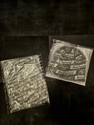 Mössa och halsvärmare  - Säljer ett set med svart och vit mössa och matchande halsvärmare från Tholmarks. Båda plaggen har ett tryckt logomönster med texten 'Since 1962". Tillverkade i mjuk polyester som passar perfekt för kyliga dagar.