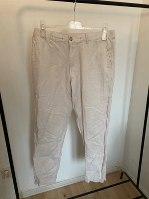 Beige Linnebyxor från Uniqlo, storlek L - Säljer ett par ljusbeige linnebyxor från Uniqlo i storlek L. Byxorna har dragsko i midjan, dragkedja och knapp, samt fickor både fram och bak. Materialet är en skön mix av bomull, linne och elastan för extra komfort. Perfekta till en clean och avslappnad stil.