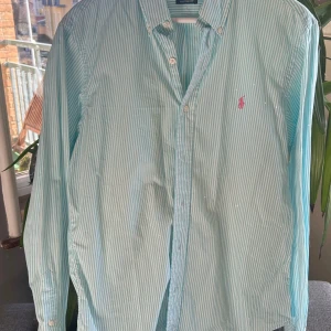 Randig skjorta från Ralph Lauren - Snygg ljusblå och vit randig skjorta från Ralph Lauren i storlek M. Skjortan är i otroligt bra skick med logga på bröstet och är långärmad med knappar framtill. Perfekt för en stilren look! Skjortan är knappt använd, hör av dig vid minsta fundering!