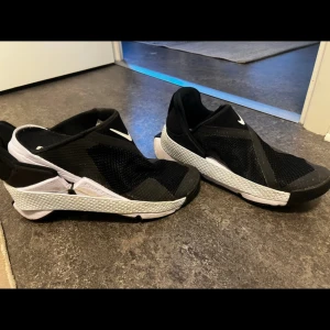 Nike Go FlyEase svarta sneakers - Använda max 3-5 gånger, Nike Go FlyEase sneakers i svart och vitt med innovativ handsfree-design. Ovandel i mesh och syntet, elastisk häl och vit sula med textur. Snygga och futuristiska skor som är lätta att ta på och av, perfekta för dig som gillar smarta detaljer och modern stil.