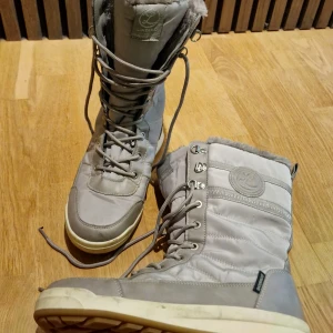 Grå fodrade vinterstövlar - Snygga grå vattentäta vinterstövlar med snörning och quiltad ovandel. Skorna har rund tå, platt sula och mjukt foder för extra värme. Perfekta för kalla dagar och har en sportig look med detaljer i syntet och mocka. Kan funka för pojkar också men finns en glittrig logo på "tungan" högst upp vid stället där man knyter snörningen.