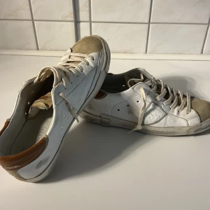 Philippe Model vita sneakers i skinn - Snygga vita sneakers från Philippe Model med beige mockadetaljer på tån och brunt skinn vid hälen. Klassisk låg modell med snörning och rund tå. Skorna har en platt sula och är tillverkade i en mix av skinn och mocka för en cool och avslappnad look.