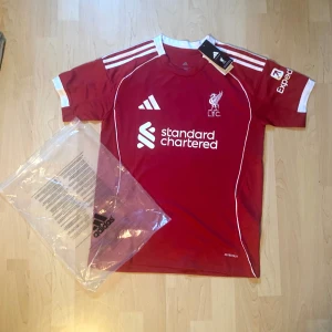 Liverpool Salah 11 matchtröja Adidas - Liverpool FCs officiella matchtröja från Adidas med M. Salah och nummer 11 på ryggen. Röd med vita detaljer, klubbmärke och sponsortryck framtill. Kortärmad modell i lätt funktionsmaterial, perfekt för fotboll eller supporterliv.