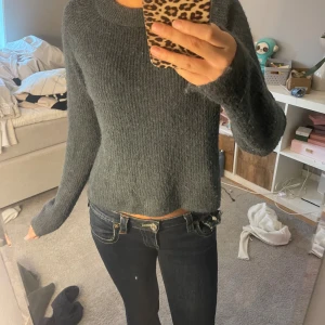 Mörkgrå stickad tröja med rund hals - Mysig mörkgrå stickad tröja med rund halsringning och långa ärmar. Tröjan har en enkel, klassisk design och är perfekt för kyligare dagar. Den är mjuk och har en lätt loose passform som gör den superbekväm att bära.