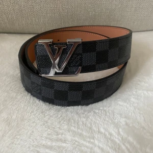 Skärp, svart 105cm - Snyggt svart bälte, klassiskt rutigt mönster och silver emblem på spännet. Bältet har bra material och mer information kan frågas.