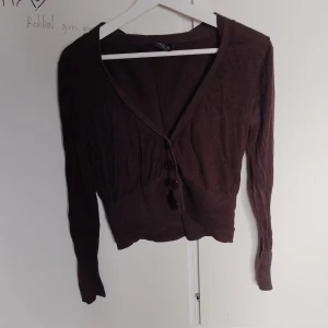 Brun kofta från August Silk - Mysig brun kofta från August Silk med v-ringning och stora knappar framtill. Långärmad och figurnära passform, perfekt att slänga över ett linne. Stickad i mjukt material som känns skönt mot huden.