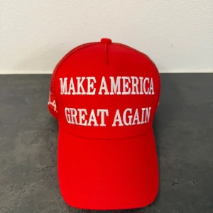Röd MAGA keps - Röd keps med vit brodyrtext 'MAKE AMERICA GREAT AGAIN' framtill, '45-47' på sidan och amerikansk flagga broderad. Baksidan har texten 'TRUMP'. Kepsen har meshpaneler och justerbar knäppning bak för skön passform.