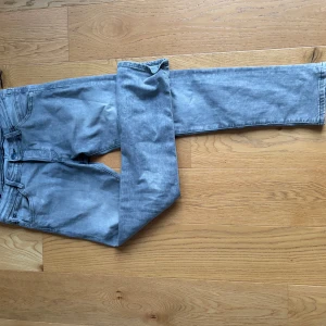 Grå slim jeans med raka ben - Säljer ett par grå jeans med slim passform och raka ben. Jeansen har klassisk femficksdesign, bälteshällor och dragkedja. Materialet är mjukt och stretchigt jeans, perfekt för en avslappnad look.