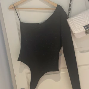 Glittrig Body med en arm - En body som är svart och glittrig från NA-KD den är helt oanvänd och i storlek M men den är väldigt tight så skulle säga att den är S - M