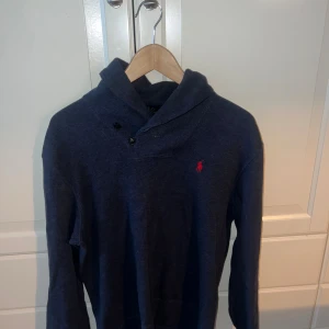 Blå tröja från Polo Ralph Lauren - Mörkblå långärmad tröja från Polo Ralph Lauren med klassisk röd logga broderad på bröstet. Tröjan har en unik krage med två knappar och är tillverkad i mjuk bomull, hör av er vid funderingar! Pris kan diskuteras.