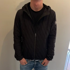 Svart quiltad jacka från Colmar - Säljer en svart quiltad jacka från Colmar med huva och dragkedja framtill. Jackan har ett stilrent mönster, Colmar-logga på ärmen och är perfekt för dig som gillar en clean look. Modellen är 168 cm lång och väger 54 kg. Passar dig mellan 160-170 Det är bara att höra av sig vid frågor och funderingar 😀