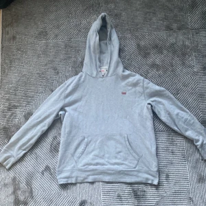 Grå hoodie från Levi's i bomull - Säljer en ljusgrå hoodie från Levi's i mjuk bomull. Klassisk modell med huva, magficka och liten röd Levi's-logga på bröstet. Passar S och XS. Utan snören 