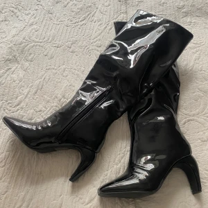Svarta lackade stövlar från NLY Shoes - Säljer ett par svarta, glansiga stövlar från NLY Shoes. De har spetsig tå, hög klack och dragkedja på insidan. Materialet är syntet med lackad finish som ger en riktigt snygg statement-look. Perfekta för dig som vill sticka ut. Oanvända nypris 699 kr 
