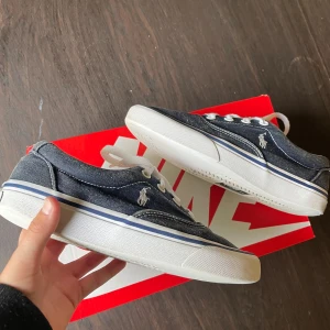 Polo Ralph Lauren Skor Stl37  -   Poli rl sneakers – begagnade   Säljer ett par Polo rl sneakers i mörk denimfärg med vit sula. Skorna är använda men i ganska bra skick. Sulorna är fortfarande hela och har bra grepp, men det finnsslitage på bakkanten med två synliga hål i fodret vid hälen.   Trots slitaget är skorna fortfarande bekväma och fullt användbara. Perfekt som vardagsskor eller som ett extra par.   Tveka inte att höra av dig om du vill ha fler bilder eller frågor?