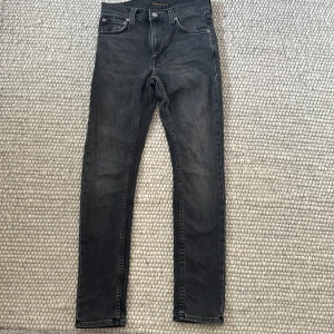 Svarta skinny jeans från Nudie Jeans - Snygga svarta jeans från Nudie Jeans med klassisk femficksdesign och diskret logga på bakfickan. Jeansen har en skinny passform och är tillverkade i stretchig denim för extra komfort. Perfekta för dig som gillar en smal siluett och mörk tvätt.