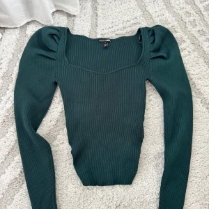 Mörkgrön ribbad topp från Fashion Nova - Säljer en mörkgrön ribbad topp från Fashion Nova i storlek S. Toppen har långärmade puffärmar, fyrkantig halsringning och är figurnära. Materialet är 80% rayon och 20% polyester, vilket gör den mjuk och stretchig. Perfekt för dig som gillar stilrena detaljer.