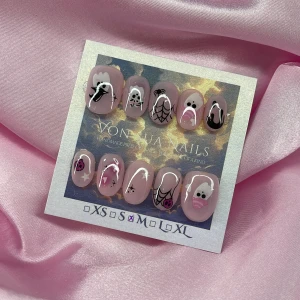 Spooky (M);ExtraShortOval  - Set med handmålade press-on naglar i en extra kort oval form med ljusrosa nude bas. Motiven är spöken, spindelnät, hjärtan, stjärnor och små detaljer i svart, vitt och rosa. M: 16 mm, 12 mm, 12,5 mm, 11,5 mm, 10 mm. Perfekt för dig som vill ha unika och kreativa naglar med halloween-vibe.