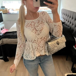 Vit spetsblus med volang  - Superfin vit blus i spets med lång ärm och volang nertill . 