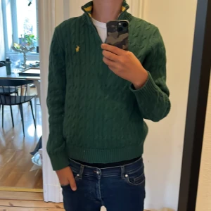 Polo Ralph Lauren quarter zip - Grön kabelstickad tröja från Polo Ralph Lauren med gul broderad logga på bröstet. Tröjan är i toppenskick, Skick 8/10 Inga defekter eller skada, Pris 699kr, Tveka inte vid frågor eller funderingar, (Priset kan diskuteras) 