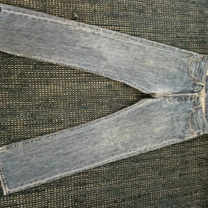Levi's 501 ljusblå jeans W32 L32 - Klassiska Levi's 501 jeans i ljusblå tvätt med raka ben och normal passform. Jeansen har fem fickor, knappgylf och ikonisk röd Levi's-tag bak. Tillverkade i slitstarkt bomullsjeans, perfekta för en avslappnad stil. Med slitage visas med bild