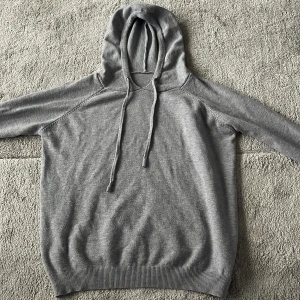 Grå hoodie med snören  - En stilren grå hoodie med huva och snörning. Tröjan är enkel att matcha med och väldigt snygg. Skick 8/10 använd några gånger men inget som syns nypris 399kr säljs för 150kr.