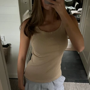 Beige ribbad linnetopp från Gestuz - Säljer en snygg beige ribbad linnetopp från Gestuz. Toppen är ärmlös med rund halsringning och har en tight passform som framhäver figuren. Perfekt att styla med jeans eller kjol för en clean och enkel look.