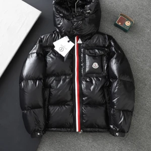 Svart pufferjacka från Moncler - Snygg svart pufferjacka från Moncler med glansig finish, huva och ikonisk logga på bröstfickan. Jackan har rödvit rand längs dragkedjan och praktiska fickor. Perfekt för kalla dagar och ger en cool streetstyle-vibe. Använd två gånger kom priv för mer bilder